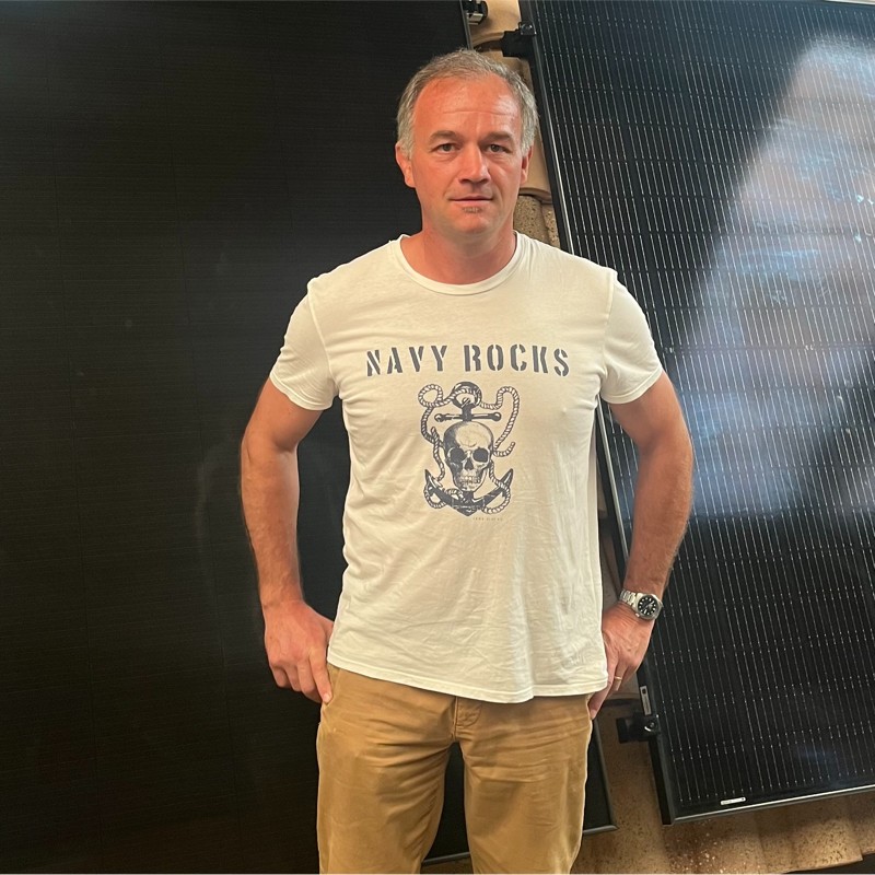 Technicien Demoury Energie à Mérignac devant panneaux solaires noirs, portant t-shirt NAVY ROCKS et pantalon beige